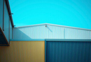 Industrial factory building features an aluminium facade with a chimney, reflecting modern architecture under a clear blue sky.