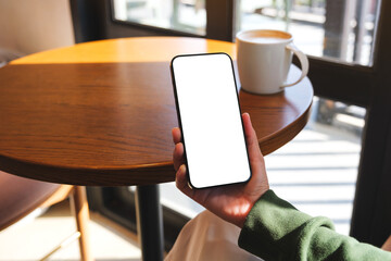 Mockup image of a woman holding mobile phone with blank desktop screen in cafe