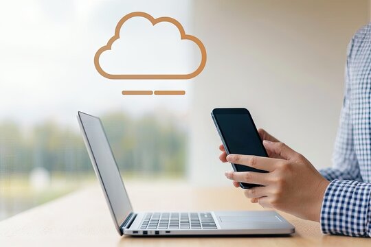 A person uses a smartphone beside a laptop with a cloud icon, symbolizing digital connectivity and cloud computing.