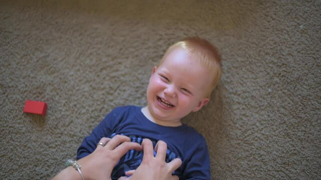 Laughing Toddler Enjoying Playful Tickles Overhead view of joyful toddler lying on carpet, laughing while being tickled by caregiver hands in warm, playful moment child laughing 