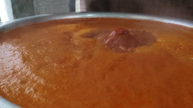 A close-up of a vibrant red sauce bubbling as it simmers, releasing rich aromas of spices and herbs. The thick texture and deep color hint at a flavorful, slow-cooked dish.
