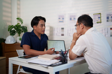 Engineers discussing construction plans at the desk with blueprints and calculators, focusing on project strategies and material estimates