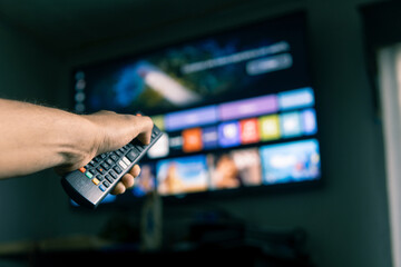 Man using remote control to choose streaming platform program on smart tv