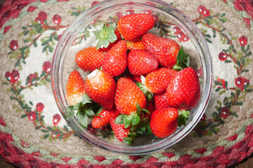 Freshly picked strawberries arranged in a glass bowl on a colorful mat