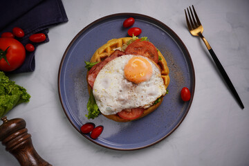 Fresh waffles with fried eggs, lettuce, tomatoes and served for breakfast on a flat table.