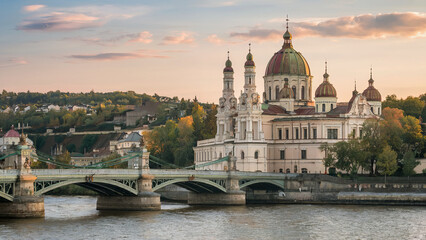 Historic church with domes and bridge over river at sunset in a scenic European cityscape