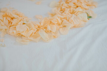 Orange rose petals placed in the shape of a heart on a white bed for newlyweds and brides