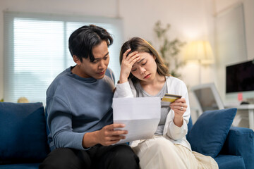 A man and woman are sitting on a couch, looking at a piece of paper
