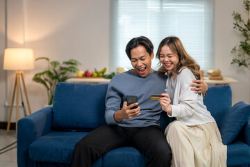 Obraz premium A man and woman are sitting on a blue couch, smiling and holding a credit card