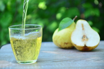 Pear juice on wooden table outdoors. Glass of juice and pears fruits, summer garden on background. Healthy summer drinks concept.