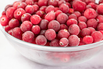 Frozen cranberries in transparent bowl, on light background. Preservation of vegetables and fruits. Natural products