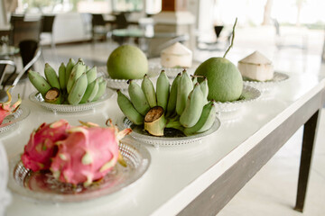 Fruits, including dragon fruit, banana, pomelo, and coconut, placed on a plate on a white wooden table
