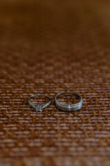 Wedding rings, two rings made of silver adorned with genuine diamonds. Groom's ring and bride's ring placed on a brown background, close-up shot