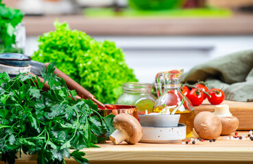 Healthy eating, cooking, food blogging background. Oak cutting board with vegetables, herbs, mushrooms and linen napkin on cozy kitchen with wooden table, kitchenware and ingredients
