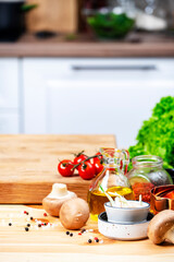 Healthy eating, cooking, food blogging background. Empty oak cutting board with mushrooms, tomatoes, lettuce, vegetables on cozy kitchen with wooden table, kitchenware and utensils