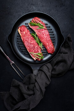 Raw beef sirloin steaks with medium mamory with rosemary on grill pan. Black background, top view