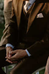 Groom in wedding suit with long sleeves. Handsome man in tux. Close up. Dark brown suit and cream tie. There was morning light falling on him