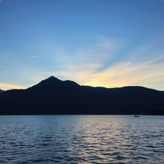 Silhouette mountain and calm lake view with blue sky in twilight, creating sense of serene, reflection of daylight on water and boat as far distance