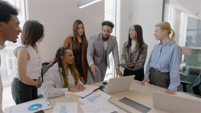 In a modern office, a diverse group of professionals engages in animated discussion around a laptop, highlighting the importance of teamwork in achieving their collective business goals