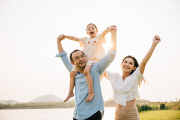 Asian family child girl piggyback riding back on father raising hands like flying outdoor nature park with mother, Happy parent daughter having fun together, Tourist lifestyle family leisure activity