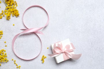 8 March, International Women's Day. Figure eight made of pink ribbon with beautiful mimosa flowers and gift box on a gray background. Space for text