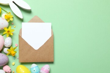 Happy Easter. Colorful eggs, yellow flowers, bunny ears and paper envelope on a pastel color background, space for text or advertising