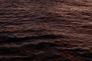 Calm, rippling water at sunset. Abstract view of the water surface at sunset. Texture with warm, golden hues. Close up