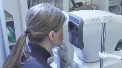 A woman undergoing an eye examination with an automatic refractometer in a clinic.