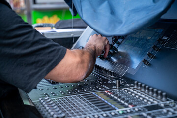 A man is working on a sound board with a blue bag on his lap. Scene is focused and determined as the man works on his project