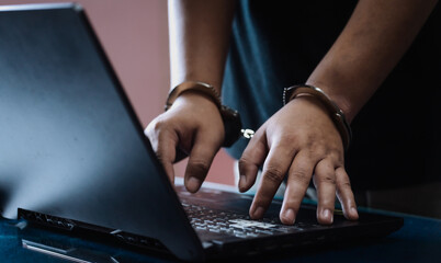 Cybercrime arrest concept. Close-up of a hacker in handcuffs typing on a laptop, symbolizing...