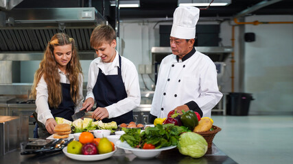 Chef teacher teaches cooking to the group children in class kitchen room.  Chef preparing student for learning marking and cooking food at workshop.  Education Concept