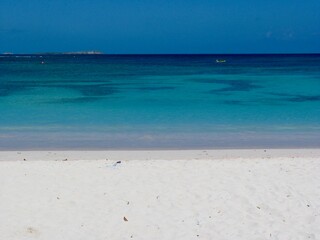 A serene tropical beach with soft white sand and crystal-clear turquoise waters stretching to the horizon. A lone kayak floats in the distance, creating a peaceful and dreamy vacation paradise.