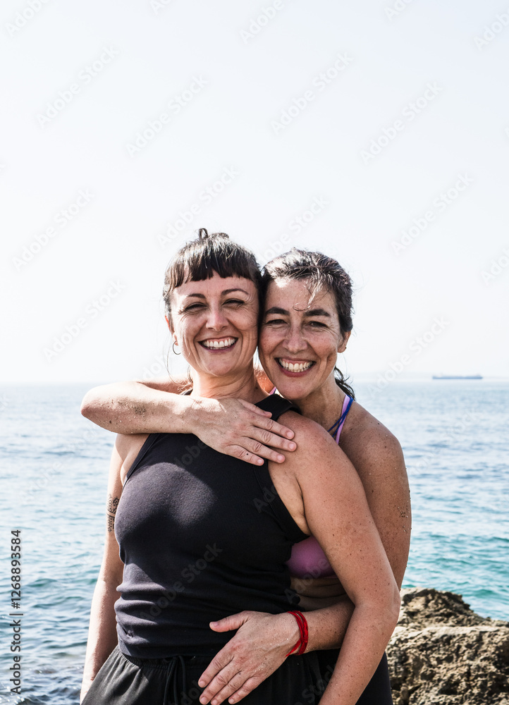 Wall mural Two joyful women embracing by the sea on a sunny day, displaying genuine happiness and friendship