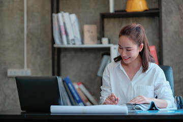 The Asian female engineer is working on her laptop at her desk.