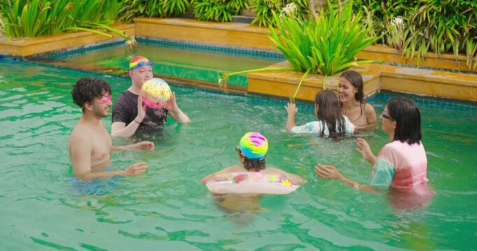 Indian wet family group cute teen child play ball game in water pool have fun joy spend day time happy mom dad male man female young adult girl kid son boy wear ring enjoy hotel trip resort park