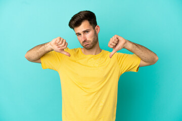 Young caucasian handsome man isolated on blue background showing thumb down with two hands