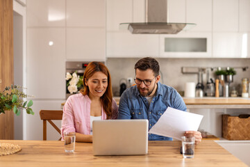Couple is sitting at a table, focused on a laptop screen. They be discussing or working together,...