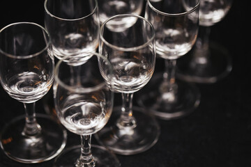 Crystal vodka glasses on a black bar counter. Elegant glassware for alcohol. Empty shot glasses ready for a celebration. Classic bar setting. Dark alcohol background. Premium nightlife drinking.