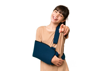 Little caucasian girl with broken arm and wearing a sling over isolated background pointing front with happy expression