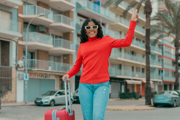 Young tourist woman walking with suitcase and making victory sign