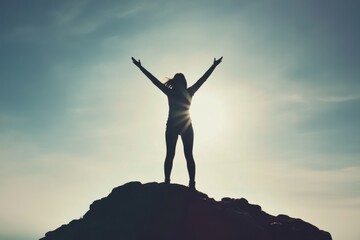 A woman standing on top of a mountain, arms raised towards the blue sky. Her silhouette exudes strength,and freedom, her flowing hair blending into the bright sky. Cocept for travel and woman power.