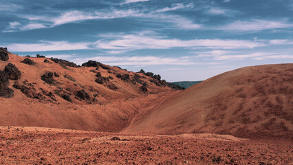 Volcanic sand arid wasteland in caldera of Tenerife during summer hot day with hills, mountains, dunes and dark black volcanic rocks. Orange sand beautifully contrast with blue sky with clouds. Spain
