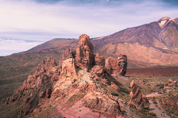 Scenic drone like view over volcanic rock formation called La Catedral with epic mountains on the background with summit of Pico del Teide during hot summer day on Tenerife nature park, Canary, Spain