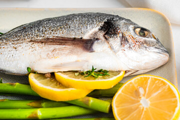 Fresh raw Dorado with asparagus spices, herbs, lemon and salt over white background.