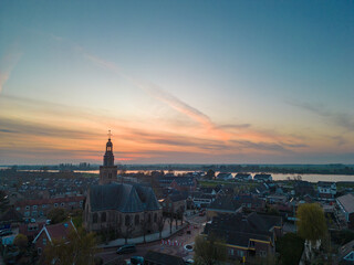 Fototapeta premium Aerial view of a Dutch Catholic church on the banks of the De Lek river in the southern Netherlands. Spring landscape with houses clustered on the vast plain of the Netherlands in the evening at sunse