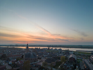 Naklejka premium Aerial view of a rural Dutch settlement on the banks of the De Lek river in the southern Netherlands. Spring landscape with houses clustered on the vast plain of Holland in the evening in Streefkerk