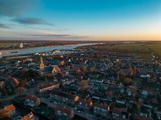 Obraz premium Aerial view of a rural Dutch settlement on the banks of the De Lek river in the southern Netherlands. Spring landscape with houses clustered on the vast plain of Holland in the evening in Streefkerk
