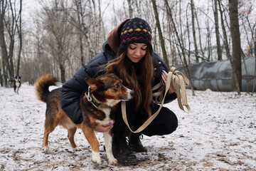 Walking a dog in a winter park. A young woman in a down jacket and hat with her pet. Love of animals