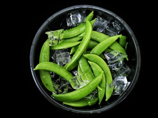 snow peas in a black bowl isolated black background