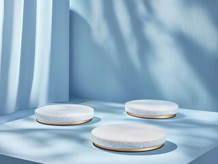 Light-filled, pale blue room with draped fabric and three round, light marble podiums